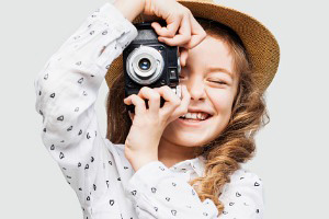 Young girl smiling taking a picture with a camera.